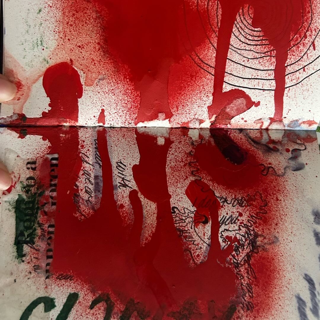 Open sketchbook spread flooded with saturated red spray, handwritten text and concentric ink circles pressing up through the surface.